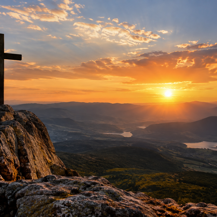 Cruz no alto de uma montanha diante do pôr do sol
